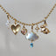 Gold necklace with various charms including a heart, cloud, and rabbit on a gray background