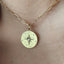 A gold chain necklace with a round pendant worn on a person's neck. The pendant is pale yellow with a starburst design, small star motifs, and a tiny central clear stone.
