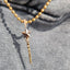 A gold-toned beaded necklace with a star-shaped pendant and a twisted spike charm, shown worn against a gray knit top.