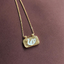 A gold pendant necklace featuring a rectangular tag-style charm with a white swan design, resting on a textured dark brown surface.