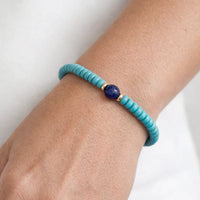 Turquoise beaded bracelet with a blue stone on a wrist against a white background