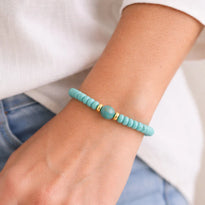 Turquoise beaded bracelet on a wrist with a white shirt and blue jeans in the background
