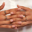 Two hands wearing gold rings on a light background