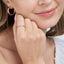 Close-up of a woman's face with gold hoop earrings and ring, touching her chin.