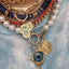 A solid gold pendant with realistic eye set in the center. Available in blue and green. Bezel set with two diamonds on the sides and spike design on the bottom.
