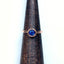 A rose gold solitaire ring with a bezel set round blue sapphire and a simple band.